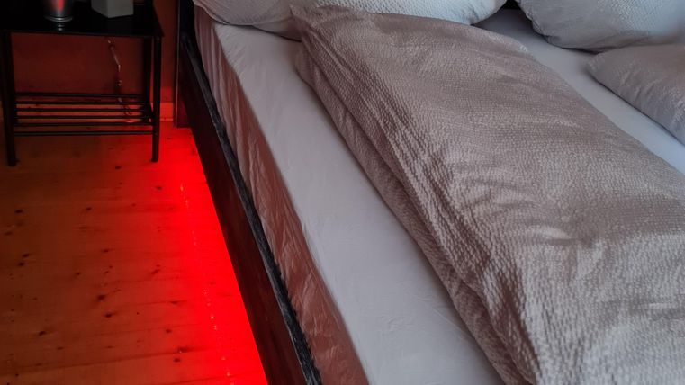 Een knusse slaapkamer met een groot bed en twee ruime kussens. Een rode verlichting onder het bed accentueert de sfeer.