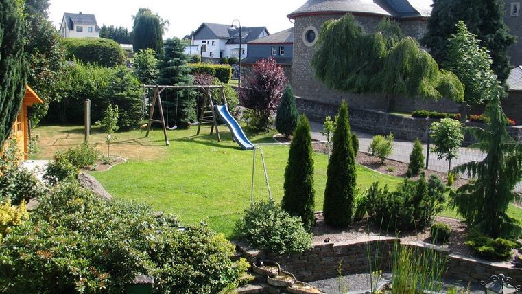 A beautiful garden with a slide and a swing. There are many plants and trees that create an inviting atmosphere.