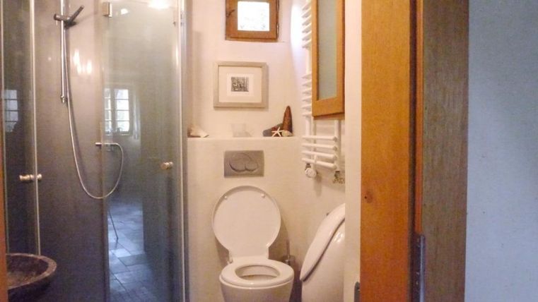 A modern bathroom with a shower and a toilet. There are windows for natural light and clean lines in the design.