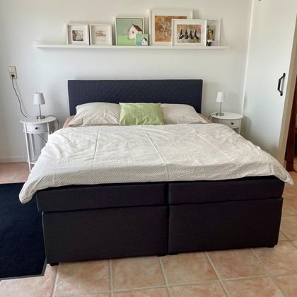 A cozy bedroom with a large bed and two nightstands. Some pictures hang on the wall above.