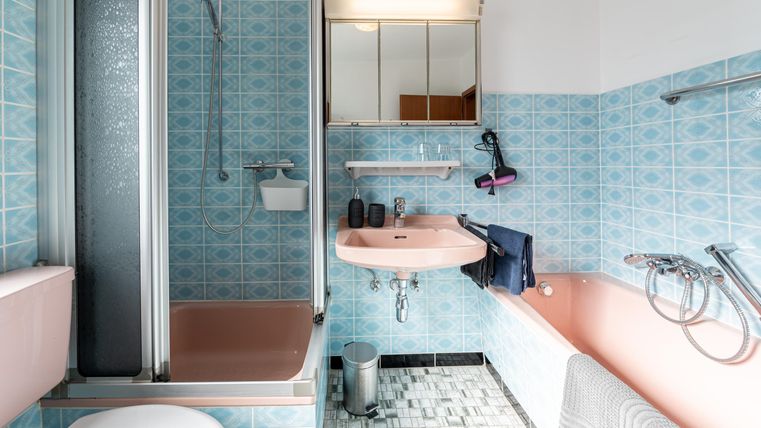 Een badkamer met een blauw tegelpatroon en roze sanitair. Er is een douche, een bad en een wastafel.