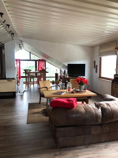 A cozy living space with a leather couch, a wooden table, and an open kitchen. Large windows provide plenty of daylight and an inviting atmosphere.