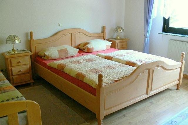 Een lichte slaapkamer met een tweepersoonsbed en twee nachtkastjes. De kamer heeft grote ramen en een warme, uitnodigende vloer.