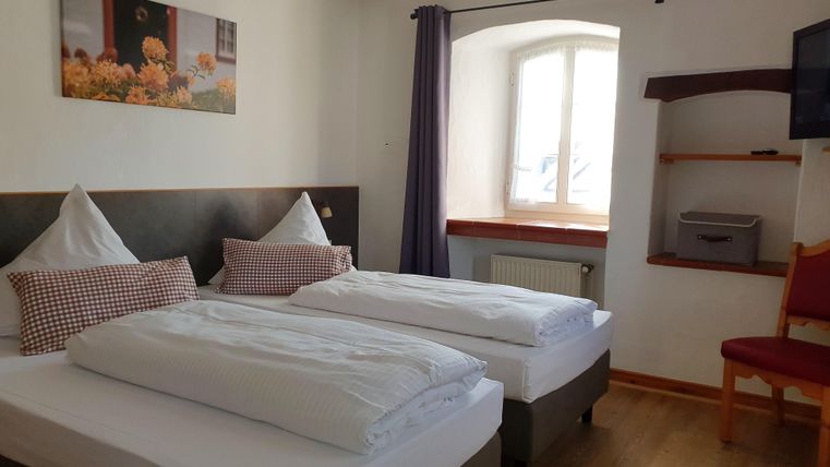 A cozy room with two single beds, decorated with pretty cushions. Large windows provide bright light and an inviting atmosphere.