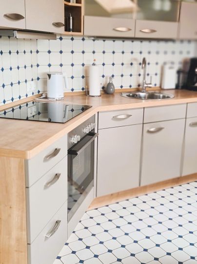 A modern kitchen with bright cabinets and a wooden countertop. The floor is designed with blue and white tiles.