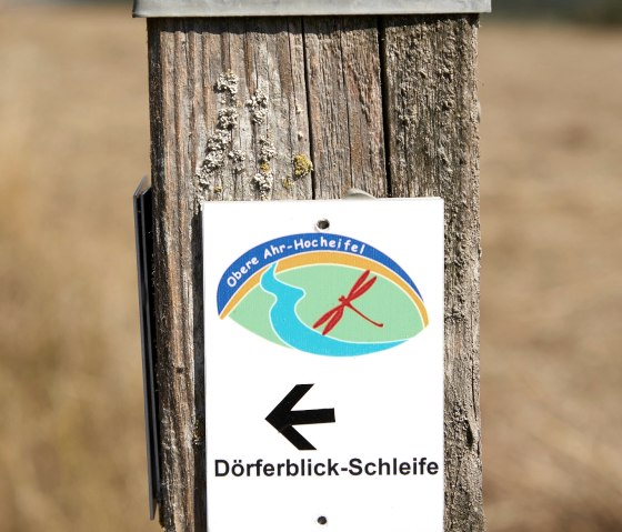 Ein Holzpfosten mit einem Schild, das die D&ouml;rferblick-Schleife in der Oberen Ahr-Hocheifel markiert. Der Pfeil zeigt nach links., &copy; VGVAdenau