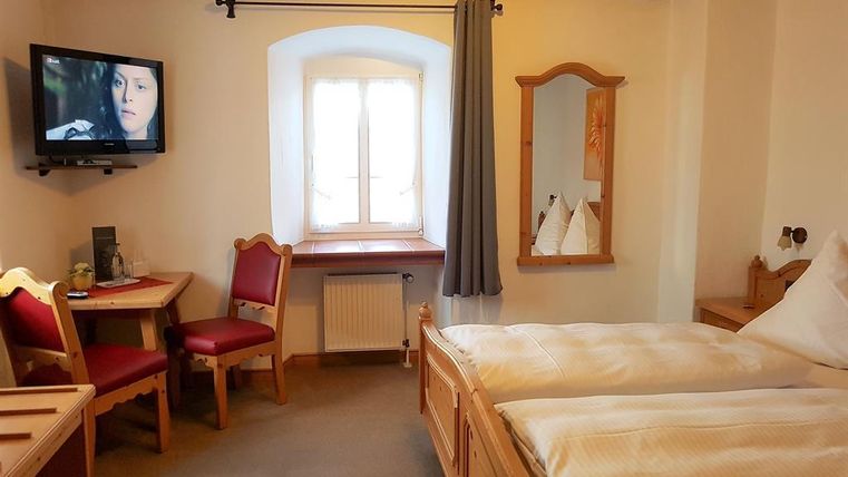 A cozy room with two beds and a television. There is a table with chairs and a window that lets in natural light.