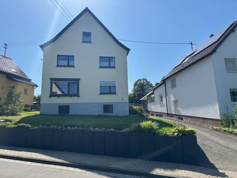 Een modern, tweeledig huis met een gele gevel staat op een groen weide. Naast het huis zijn verdere woongebouwen te zien.