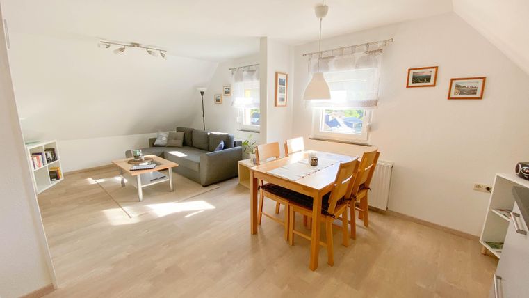 A bright and cheerful living room with a comfortable sofa and a dining table. Large windows provide plenty of daylight.