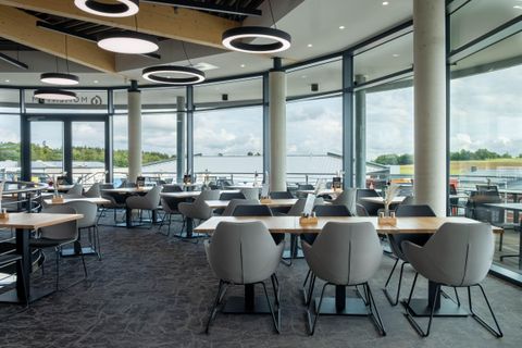 Ein modernes Restaurant mit großen Fenstern und viel natürlichem Licht. Die Tische sind elegant gedeckt und die Stühle laden zum Verweilen ein.