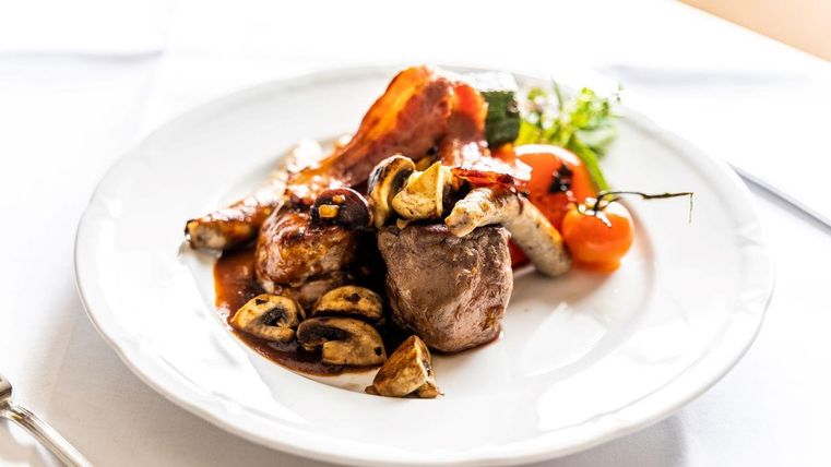 Een smakelijk bord met vlees, gebakken spek en verschillende groentegerechten. Het gerecht is kunstig opgediend en ziet er zeer lekker uit.