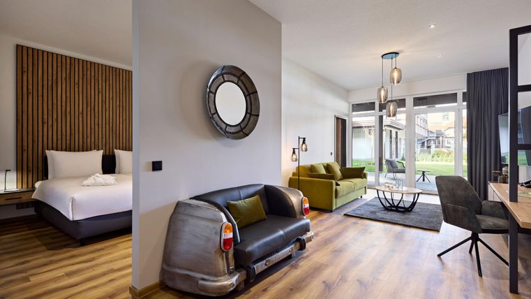 Een moderne kamer met een gezellige zithoek en stijlvolle meubels. Grote ramen bieden uitzicht op een groene tuin.