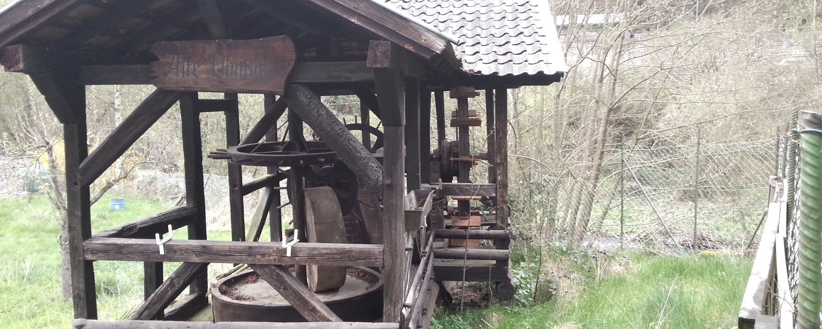 Een oude houten oliemolen met een klein dak staat in een groene, overwoekerde omgeving., &copy; Ti Hocheifel-N&uuml;rburgring
