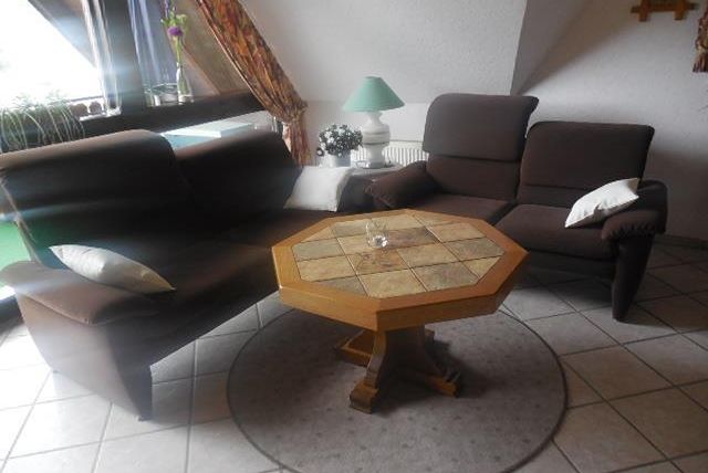 Un espace de vie confortable avec deux canapés marron et une table ronde au centre. Sur la table se trouve un petit vase en verre et en arrière-plan, il y a des fenêtres avec des rideaux.