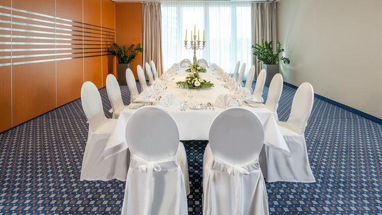 An elegant event space with a long table, set up festively. Around the table are white chairs with covers.
