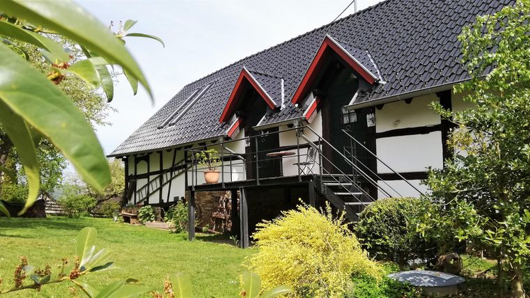 A charming half-timbered house with red-and-white accents in a green garden. The terrace invites relaxation.