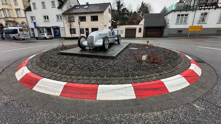 Een rotonde met een voertuigmodel in het midden. Rondom het standbeeld bevinden zich grijze stenen en een gekleurde rand.