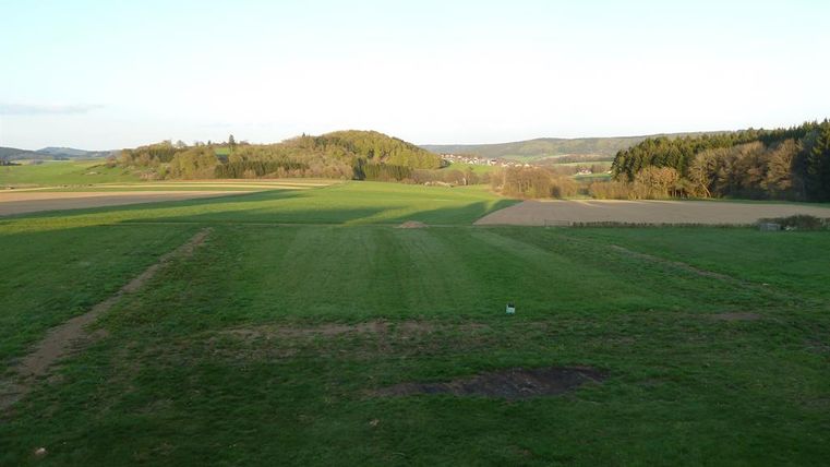 Eine weitläufige Landschaft mit sanften Hügeln und grünen Feldern. Der Himmel ist klar und es ist eine ruhige, natürliche Umgebung.