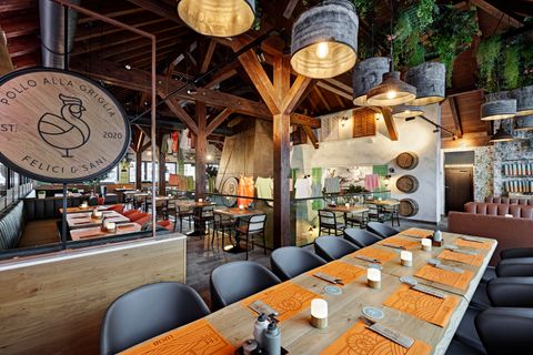 Ein modernes Restaurant mit rustikalem Holzdekor. Der große Tisch ist schön gedeckt und im Hintergrund sind Koch- und Essbereiche zu sehen.