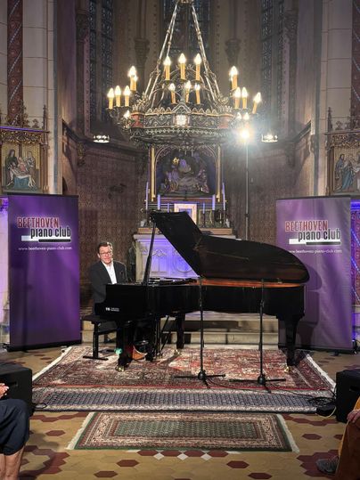 A pianist is playing piano in a festive space with church architecture. In the background, banners of the Beethoven Piano Club can be seen.