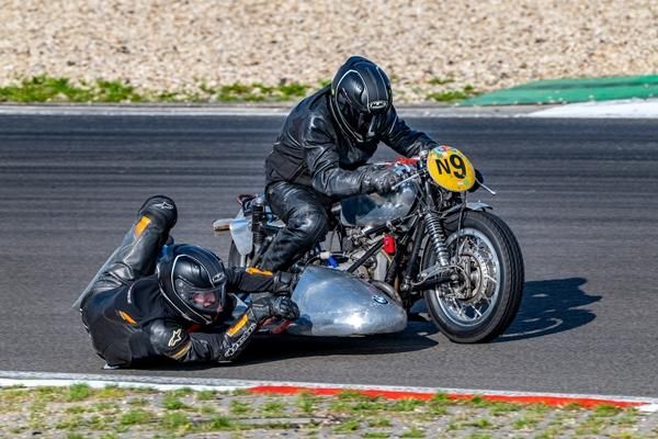 Ein Motorradrennfahrer in Lederanzug und ein Sozius auf einem Rennmotorrad. Der Fahrer ist in einer Kurve und zeigt eine actionreiche Fahrtechnik.