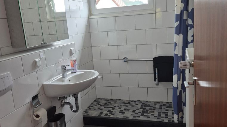A modern bathroom with white tiles and a large mirror. The shower is equipped with a blue shower curtain and a matte black floor.