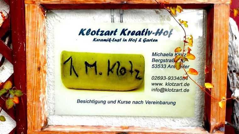 Een bord met de naam "Klotzart Creatieve Hof" en contactinformatie. Er is een creatieve verwijzing naar keramiekcursussen in de hof en tuin.
