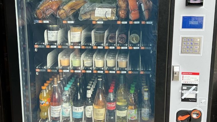Un distributeur automatique avec une variété de collations et de boissons. La sélection comprend des sandwichs, des bonbons, des boissons gazeuses et des boissons alcoolisées.