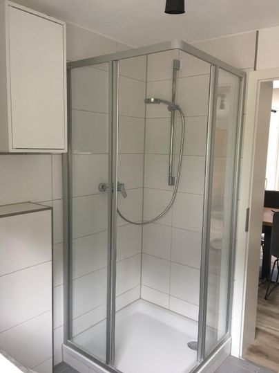 Une douche moderne avec des murs en verre et une douche à main. L'espace est lumineux et de design simple.