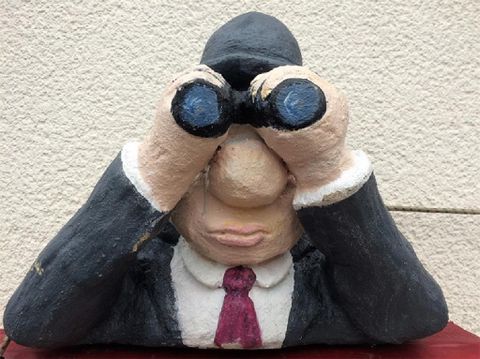 Eine Statue eines Mannes im Anzug, der mit einem Fernglas schaut. Er hat eine nachdenkliche Miene und sitzt auf einem Tisch.