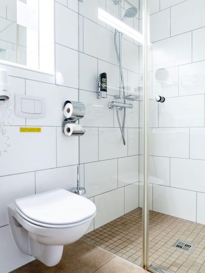 Een moderne badkamer met een douche en een toilet. De muren zijn betegeld en het licht is helder en uitnodigend.