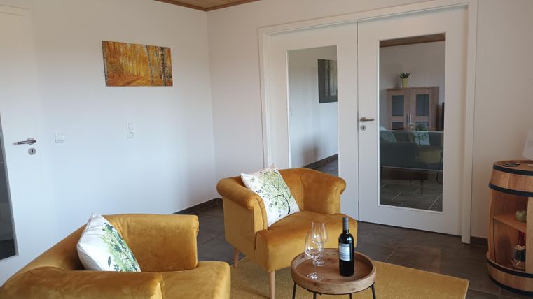 Gezellige woonkamer met twee gele stoelen en een kleine tafel. Op de achtergrond is een deur en een fles wijn op tafel.