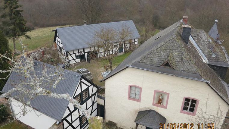A view of two traditional half-timbered houses and a modern building in a rural setting. In the background, gentle hills and trees can be seen.