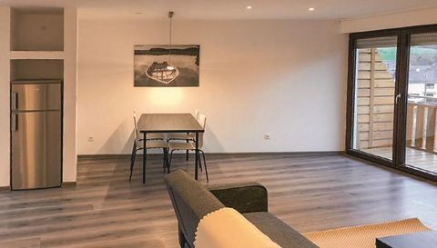 A modern and bright living room with a table and chairs. Large windows provide access to a balcony.