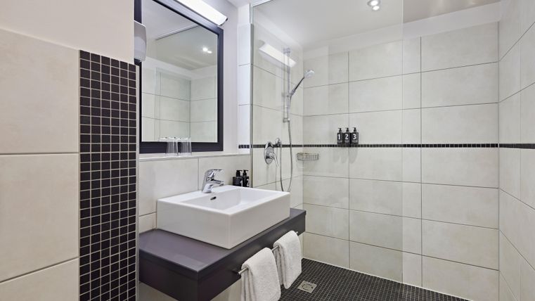 A modern bathroom with bright tiles and an elegant shower. The sink area has a stylish, minimalist design.