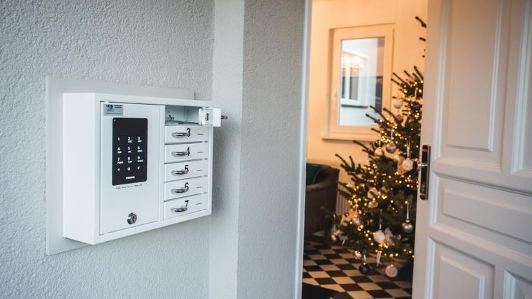 Ein briefkasten an der Wand neben einer offenen Tür. Im Hintergrund ist ein geschmückter Weihnachtsbaum zu sehen.