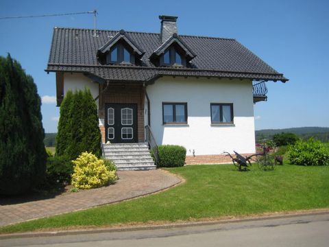 A pretty house with a black roof and white walls. The garden is well-kept and surrounded by green plants.