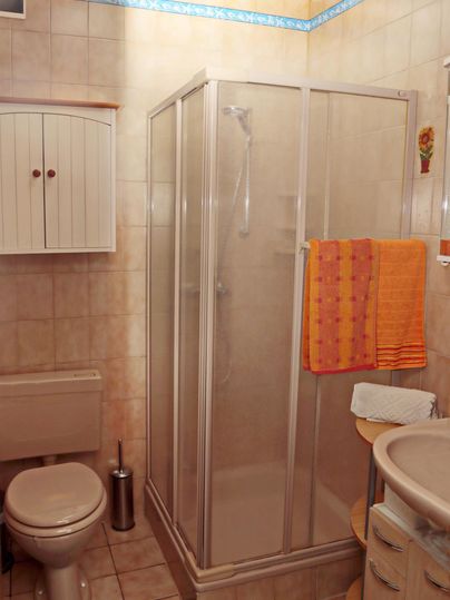 Een kleine badkamer met een douche en een wc. De muren zijn betegeld en er is een oranje handdoek.