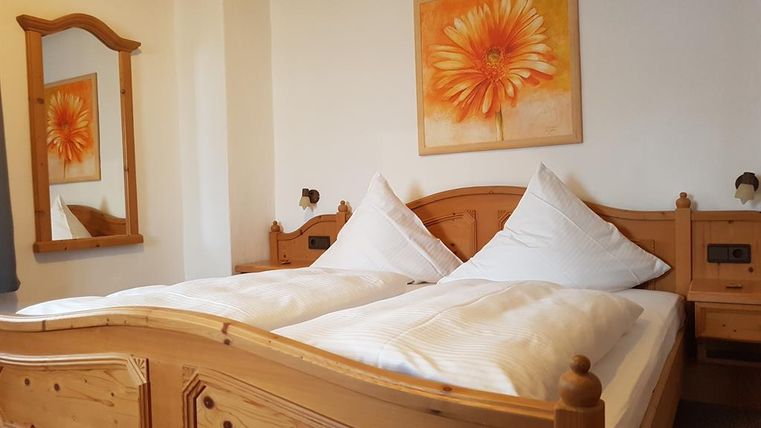 A cozy bedroom with a wooden bed and white pillows. An orange painting of a flower hangs on the wall.