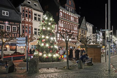 Ein festlich geschmückter Weihnachtsbaum steht in einer verschneiten Stadt. Die Lichter und roten Geschenke verleihen der Szene eine gemütliche Atmosphäre.