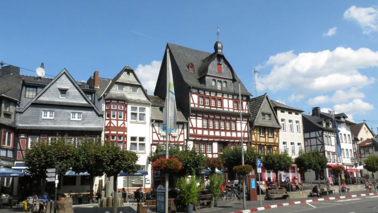 Eine malerische Stadtansicht mit charmanten alten Gebäuden. Die Straße ist von Bäumen und bunten Blumen geschmückt.