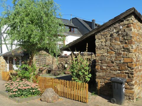 Ein schöner, idyllischer Innenhof mit einem Steinhaus und üppiger Vegetation. Im Hintergrund ist ein kleiner Garten mit einem Holzzaun zu sehen.