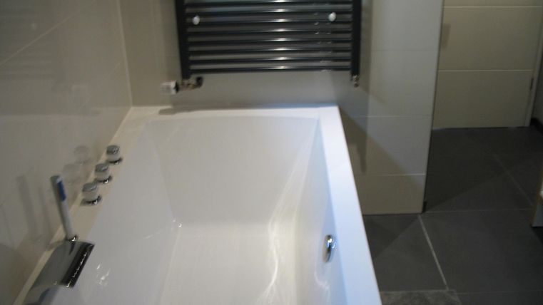 Ein modernes Badezimmer mit einer weißen Badewanne und einem handtuchwärmer. Der Boden ist mit grauen Fliesen ausgelegt.