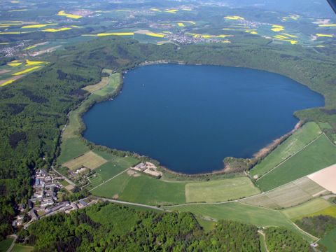 Ein großer, ovaler See umgeben von grünen Wäldern und Feldern. In der Nähe ist ein kleines Dorf zu sehen.