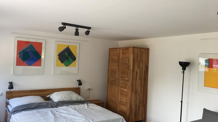 Une chambre lumineuse avec un lit double et des peintures modernes sur le mur. La pièce est équipée d'une armoire en bois et d'une lampe sur pied.