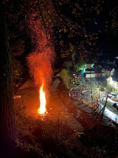 Ein großes Feuer brennt bei Nacht, umgeben von Funken. Im Hintergrund sind Gebäude und Straßenbeleuchtung sichtbar.