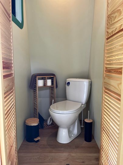 Une salle de bain moderne avec des toilettes blanches et des accessoires en bois. Les murs sont de couleurs douces et il y a une ambiance chaleureuse.