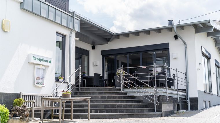 Een modern restaurant met een uitnodigend terras. De stappen leiden naar de ingang, omringd door een vriendelijke omgeving.