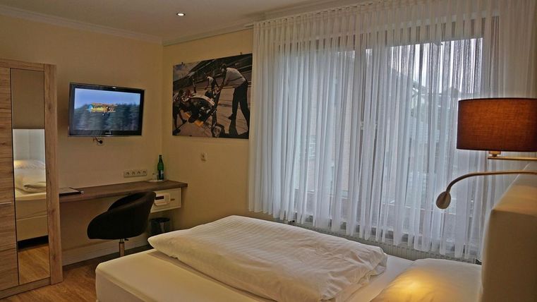 Une chambre moderne avec un lit double, un bureau et une télévision. De grandes fenêtres avec des rideaux laissent entrer beaucoup de lumière naturelle.