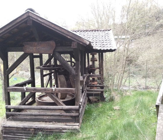 Eine alte h&ouml;lzerne &Ouml;lm&uuml;hle mit einem kleinen Dach steht in einer gr&uuml;nen, bewachsenen Umgebung., &copy; Ti Hocheifel-N&uuml;rburgring